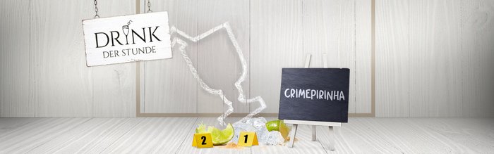 Ein hängendes Schild mit der Aufschrift 'DRINK DER STUNDE' über einem Tisch mit Limetten und Eiswürfeln.