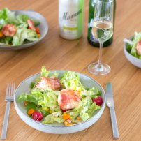 Ein gedeckter Tisch mit frischem Salat, dekoriert mit Speck und buntem Gemüse, umgeben von Gläsern und Getränken.