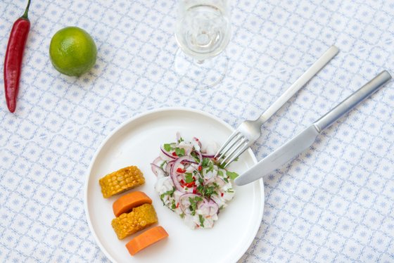 Der Fischsalat auf dem Teller wird von einer Gabel und einem Messer begleitet, während frische Zutaten wie Limette und Chili sichtbar sind.