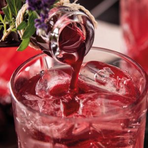 Ein roter Sirup wird aus einer Flasche in ein Glas mit Eis gegossen, um einen erfrischenden Drink zu kreieren.