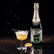 Ein stilvolles Getränk in einem Glas, umgeben von glitzerndem Konfetti und einer Flasche Sekt im Hintergrund.