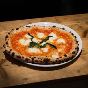 Eine frisch gebackene Pizza mit goldbraunem Rand, belegt mit Tomatensauce, Mozzarella und frischem Basilikum.