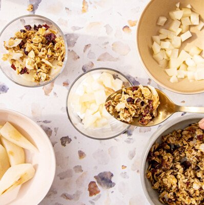 Auf einem marmorierten Tisch liegen Schalen mit Müsli und frischen Äpfeln, die appetitlich angerichtet sind.