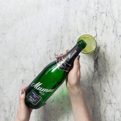 Eine Flasche Mumm Sekt wird von einer Hand gehalten, während ein Glas mit einer Limettenscheibe daneben steht.