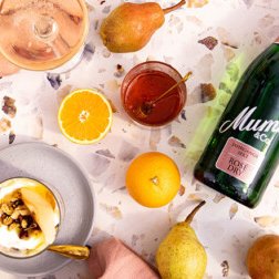 Auf dem Tisch liegen eine Flasche Mumm, frische Früchte und ein köstliches Dessert, das mit Nüssen und Karamell garniert ist.