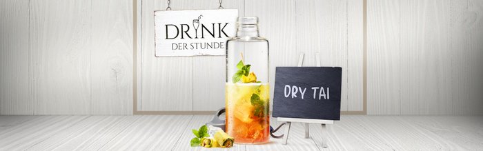 Die Flasche mit dem bunten Drink steht auf einem hellen Holztisch, während ein Schild den Namen des Cocktails präsentiert.