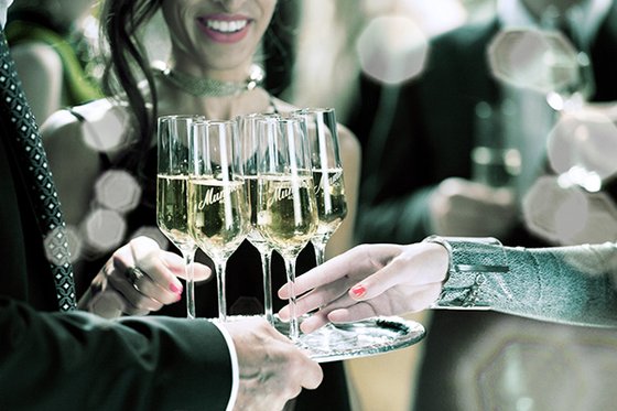 In einem festlichen Ambiente werden Gläser mit prickelndem Sekt von einer Hand an eine andere übergeben.