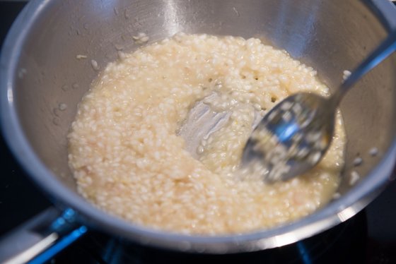 Der Topf enthält eine schaumige Risotto-Mischung, die mit einem glänzenden Löffel umgerührt wird, bereit zum Servieren.