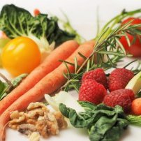 Auf einem Tisch liegen frische Karotten, Himbeeren, Spinat und Walnüsse, die eine gesunde Mahlzeit symbolisieren.