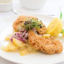 Zwei knusprige, goldbraune Schnitzel liegen auf einem Teller, umgeben von frischen Äpfeln und Zwiebeln.