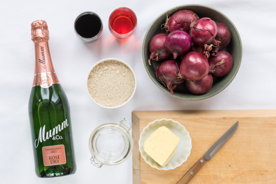 Eine Flasche Mumm Sekt steht neben einer Schüssel mit roten Zwiebeln und verschiedenen Zutaten auf einem Holzbrett.