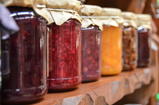 Eine Reihe von bunten Einmachgläsern steht auf einem Holzregal, gefüllt mit verschiedenen Marmeladen und Konfitüren.