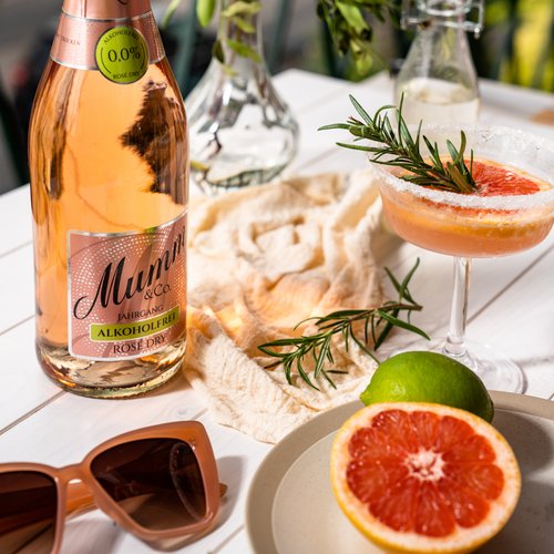 Eine Flasche alkoholfreier Rosé-Sekt steht auf einem Tisch, umgeben von frischen Kräutern und einer stilvollen Cocktailglas.
