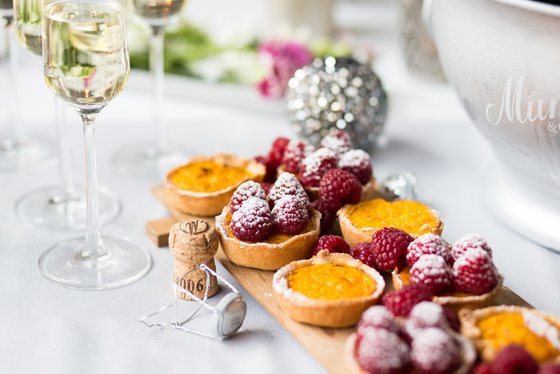 Ein elegantes Arrangement von fruchtigen Tartes mit Himbeeren und einer spritzigen Getränkewahl auf einem festlichen Tisch.