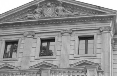Die Fassade eines historischen Gebäudes mit Säulen und Fenstern, verziert mit einem kunstvollen Relief an der Spitze.
