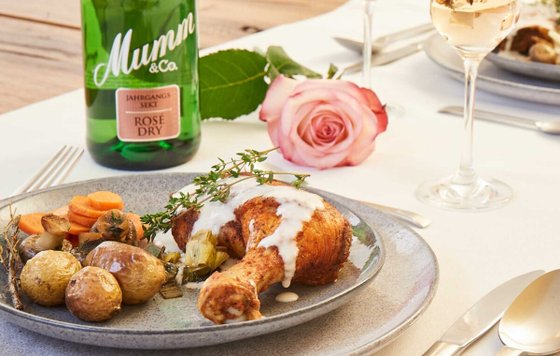 Ein rustikales Gericht mit Hähnchenkeule, Kartoffeln und Karotten, dekoriert mit frischen Kräutern und einer Rose im Hintergrund.