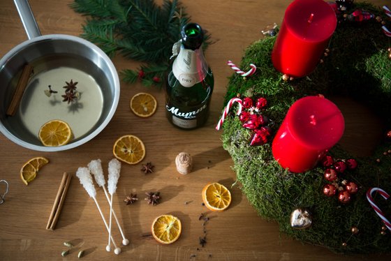 Ein festlicher Tisch mit einem grünen Adventskranz, roten Kerzen und dekorativen Elementen wie Zimt und getrockneten Orangen.