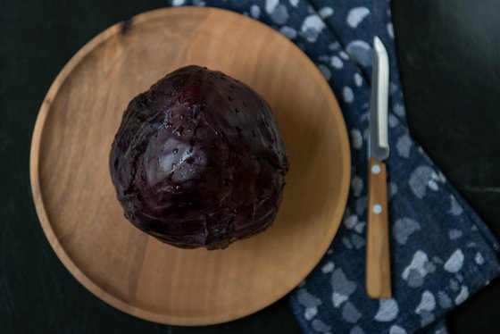 Auf einem Holzbrett ruht ein frischer, lila Rotkohl, während ein scharfes Messer daneben bereitliegt.
