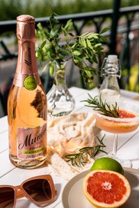 Eine Flasche alkoholfreier Rosé-Sekt steht auf einem Tisch, umgeben von frischen Kräutern und einer stilvollen Cocktailglas.