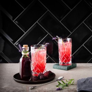 Zwei hohe Gläser mit einem erfrischenden, pinken Getränk, garniert mit Lavendel und Beeren, stehen auf einer eleganten Tischoberfläche.