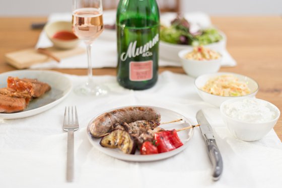Ein gedeckter Tisch mit einer Auswahl an köstlichen Speisen, darunter gegrillte Würstchen und frisches Gemüse.