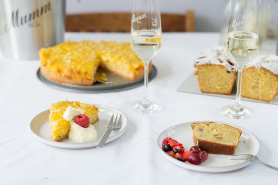 Ein Stück Ananaskuchen mit Sahne und einer Himbeere auf einem Teller, daneben frische Beeren und ein Stück Kuchen.