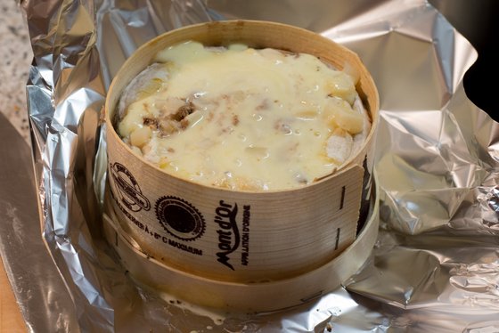 Der Holzbehälter enthält eine cremige Käseschicht, die über zarten Fleischstücken und Kartoffeln liegt, bereit zum Servieren.