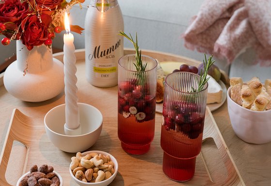 Ein stilvolles Arrangement mit Snacks, einer Flasche alkoholfreiem Sekt und zwei dekorativen Gläsern auf einem Tisch.