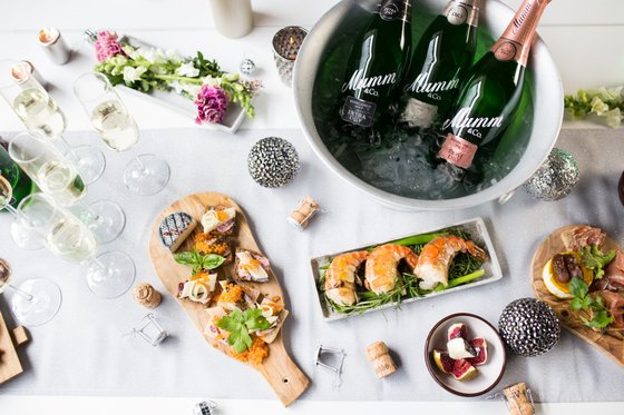 Ein eleganter Tisch mit verschiedenen Delikatessen, darunter Meeresfrüchte, Käse und frische Kräuter, umgeben von Gläsern Sekt.