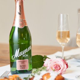 Eine Flasche Mumm Rosé Sekt steht auf einem Tisch, umgeben von zwei Gläsern und einer rosa Rose.