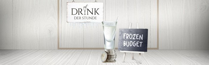 Ein Glas mit sprudelndem Getränk steht auf einem Stapel Münzen, während ein Schild mit 'Frozen Budget' daneben steht.