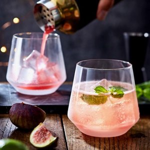 Zwei stilvolle Gläser mit einem pinken Cocktail, während ein Barkeeper das Getränk in ein Glas gießt, umgeben von frischen Feigen.