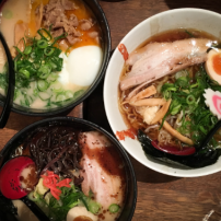 Drei Schalen Ramen mit verschiedenen Zutaten, darunter zarte Fleischscheiben, Gemüse und ein weichgekochtes Ei.