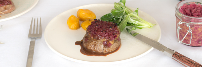 Ein saftiges Stück Rinderfilet, garniert mit Zwiebeln, serviert mit gelben Kartoffeln und frischem Salat auf einem weißen Teller.