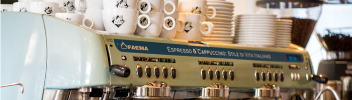 Ein Blick auf eine hochwertige Kaffeemaschine, die von weißen Tassen umgeben ist, vermittelt den Eindruck eines geschäftigen Cafés voller Leben.