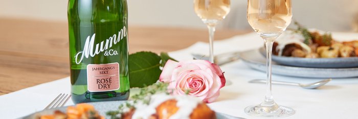 Eine Flasche Mumm Sekt steht neben zwei Gläsern, die mit sprudelndem Rosé gefüllt sind, auf einem eleganten Tisch.