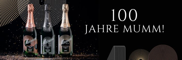Drei Flaschen Mumm Sekt stehen auf einem glänzenden Tisch, umgeben von glitzerndem Konfetti und festlicher Dekoration.