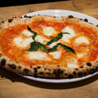 Eine frisch gebackene Pizza Margherita mit goldbraunem Rand, belegt mit Tomatensauce, Mozzarella und frischem Basilikum.