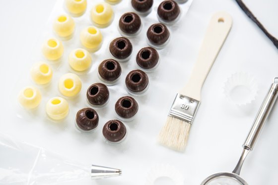 Eine Anordnung von gelben und braunen Schokoladenformen auf einer weißen Oberfläche, umgeben von Backutensilien.