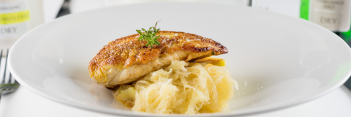 Ein saftiges Stück gebratenes Hähnchenfilet liegt auf einem Bett aus zartem Sauerkraut, garniert mit frischen Kräutern.
