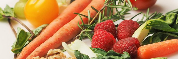 Eine bunte Anordnung von frischem Gemüse, darunter Karotten, Himbeeren und aromatische Kräuter, auf einem hellen Untergrund.