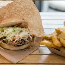 Das Sandwich ist gefüllt mit saftigem Fleisch und frischem Gemüse, daneben liegen knusprige Pommes frites auf einem Teller.