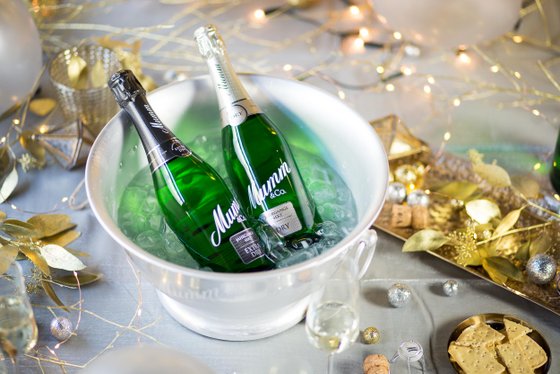 Zwei Flaschen Mumm-Sekt stehen in einem Eiskübel, umgeben von festlicher Dekoration und glitzernden Lichtern.