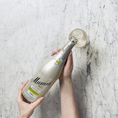 Eine Hand hält eine Flasche Mumm Sekt, während ein Glas mit sprudelndem Inhalt auf einer eleganten marmorierten Oberfläche steht.