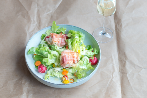 Ein frischer Salat mit knackigem Kopfsalat, bunten Karottenstücken und Radieschen, garniert mit zwei gefüllten Hähnchenbruststücken.