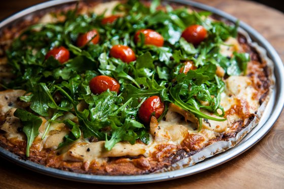 Eine frisch gebackene Pizza mit knusprigem Rand, belegt mit Rucola und saftigen Kirschtomaten, auf einem Holzuntergrund.