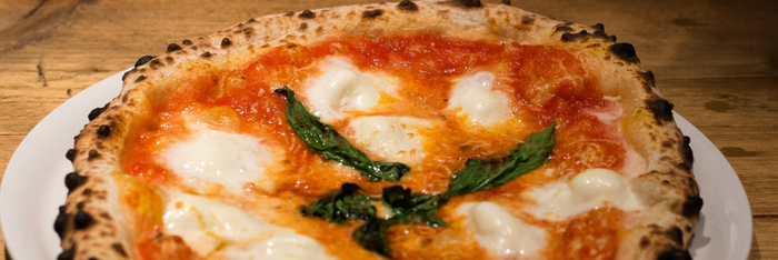 Eine frisch gebackene Pizza mit knusprigem Rand, belegt mit Tomatensauce, Mozzarella und frischem Basilikum.