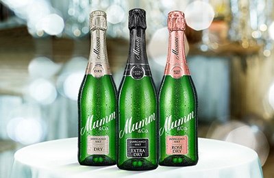 Drei Flaschen Mumm Sekt stehen auf einem Tisch, jede mit einem anderen Etikett: Dry, Extra Dry und Rosé Dry.