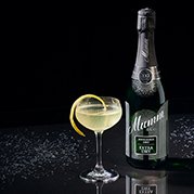 Eine elegante Flasche Sekt steht neben einem stilvollen Glas mit einem Spritzer Zitrone, auf einem glänzenden Tisch.