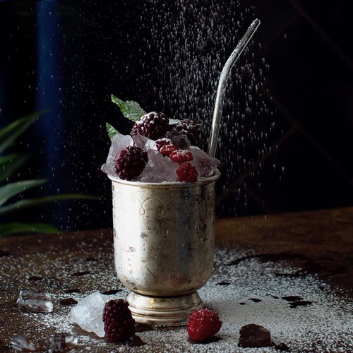 Ein silberner Becher gefüllt mit zerstoßenem Eis und frischen Himbeeren, umgeben von einer feinen Zuckerschicht.